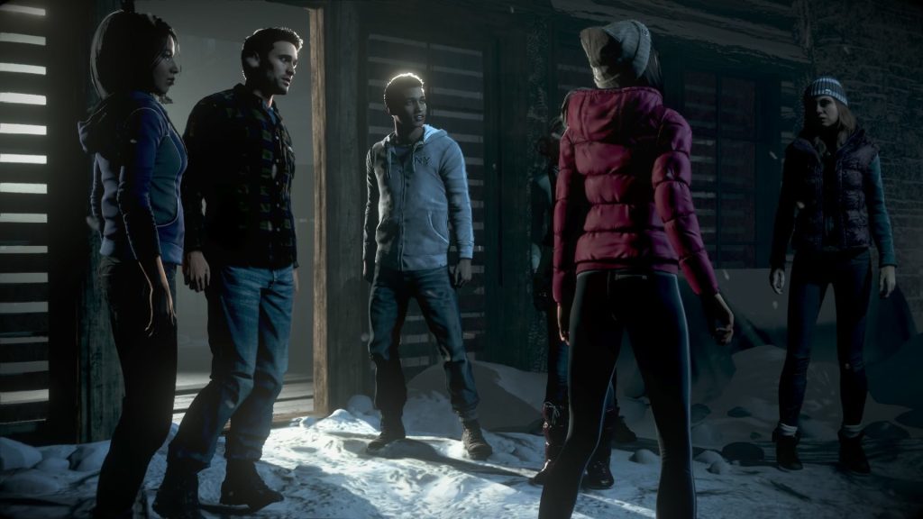 A photorealistic image of a group of teenagers- the game's protagonists- standing in the snow outside a cabin. A dark-haired young woman and a young man with short hair stand to the left of the image. An androgynous person in a grey hoodie stands in the middle; they're backlit, so light glows around the top of their head. A young woman with her back to us stands to the right; she's wearing a puffy red jacket.