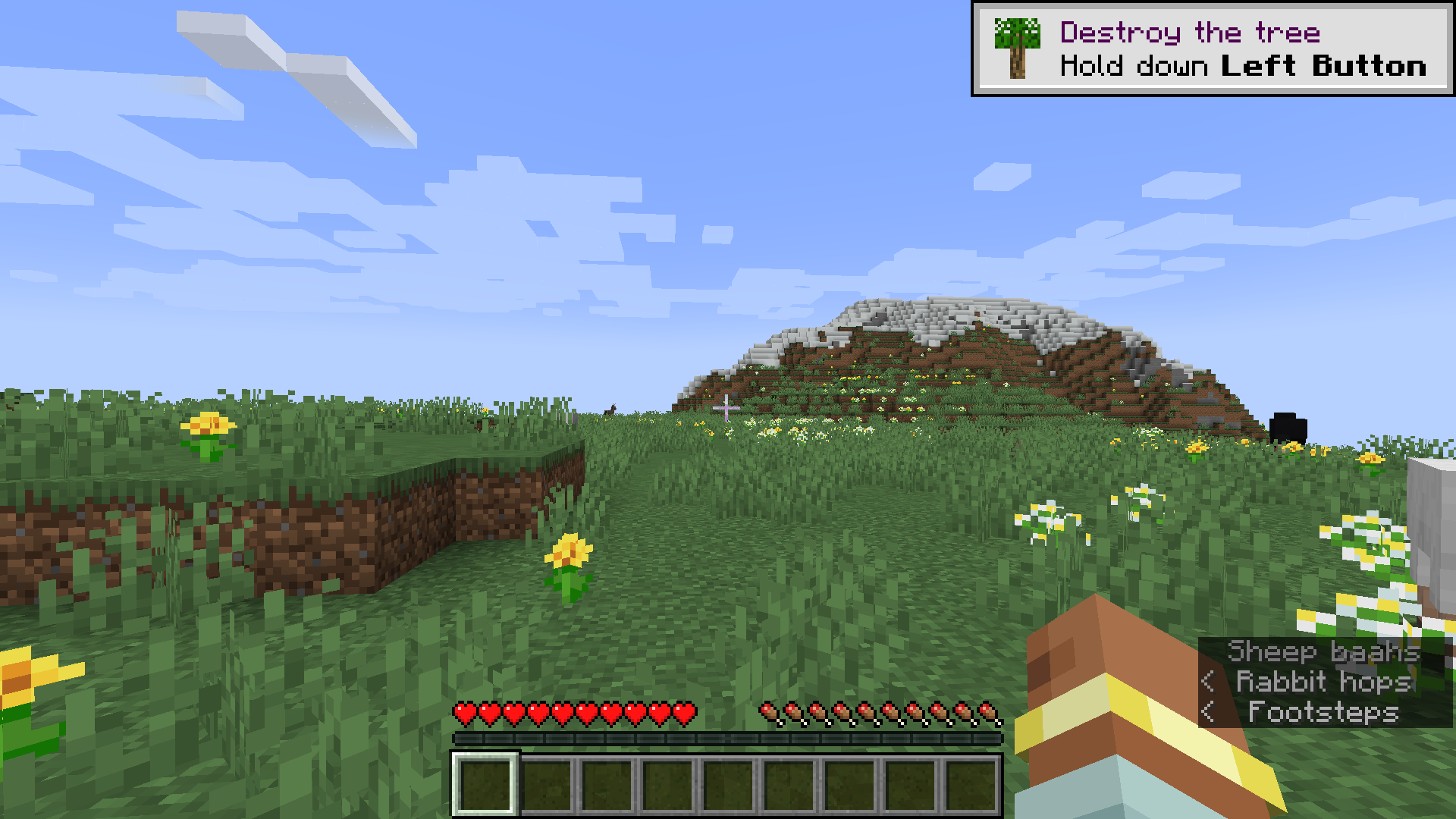 An image from Minecraft of the meadow biome with a mountain in the distance. The HUD and the player's hand are at the bottom of the screen. Captions at the right-hand side of the screen show sounds, including a sheep baa-ing and a bunny hopping.