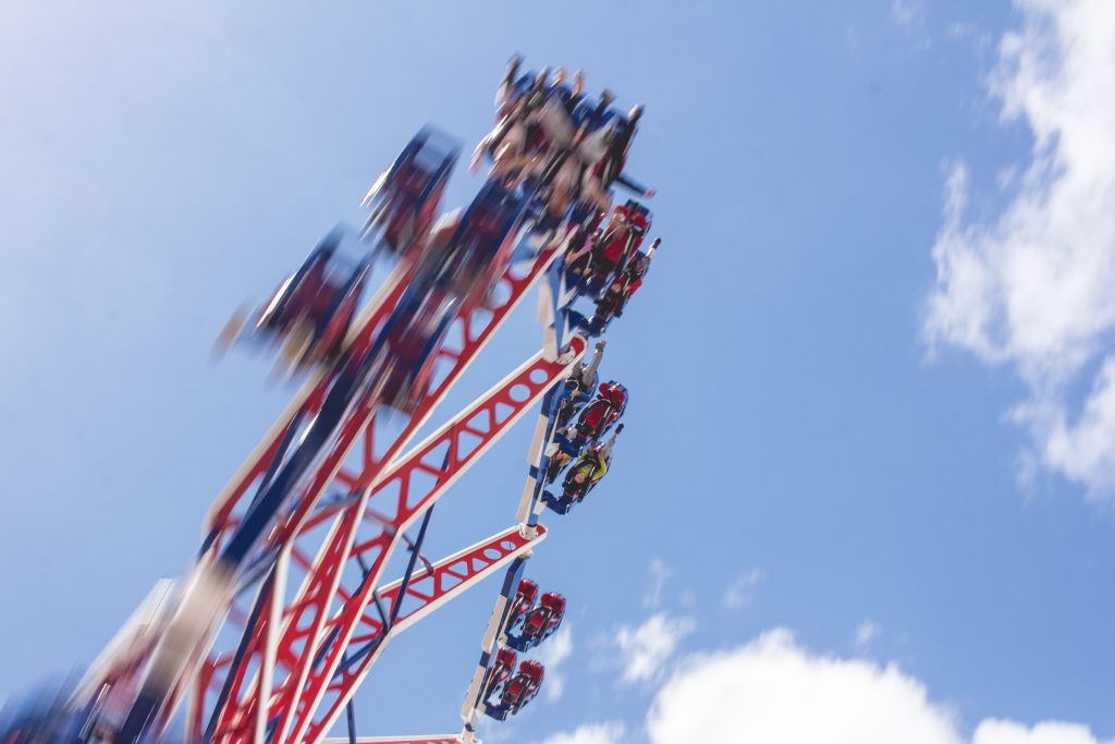 A photograph of a carnival in motion, seen from below. The ride is red, white, and blue, and is blurry from being in motion. 